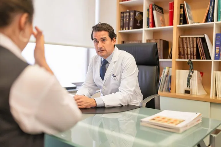 Dr. César Casado Sánchez, cirujano plástico experto en procedimientos faciales y corporales, atendiendo a un paciente en su consulta médica.